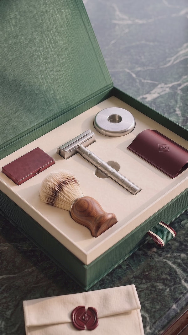The First Set unboxing: the emerald box lies open on green marble and a hand lifts the steel razor from the cream tray